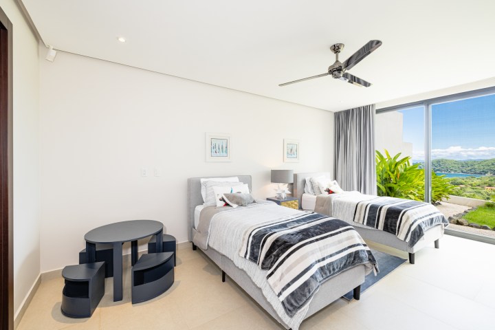 Minimalist bedroom with two single beds, large window with scenic view, and a ceiling fan.