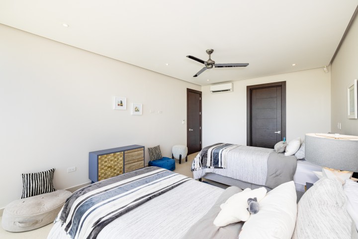 Modern bedroom with two beds, striped linens, ceiling fan, and light walls.