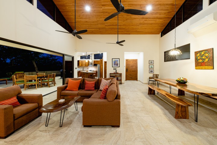 Spacious living room with brown sofas, wooden ceiling, and dining area, featuring large windows at night.