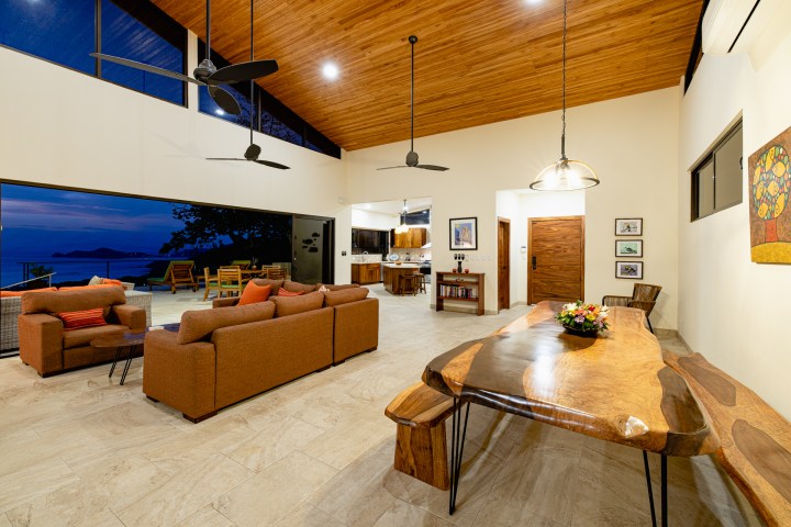 Spacious modern living room with open layout, wooden ceiling, ocean view, and stylish furnishings.