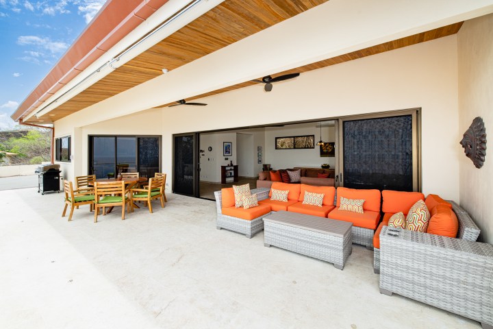 Outdoor patio with orange cushioned sofa, wooden dining set, and sliding glass doors.
