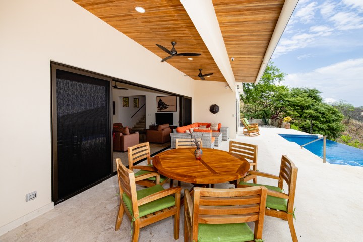 Patio with wooden dining set, ceiling fans, and pool overlooking greenery.