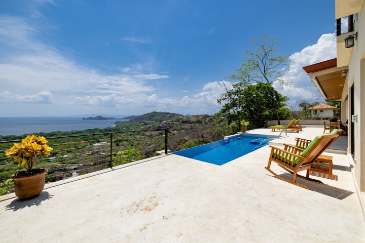 Terrace with pool, lounge chairs, and ocean view under a clear blue sky.