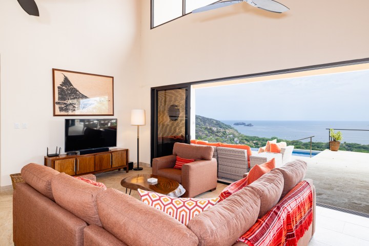Living room with brown sofas, TV, large window view of ocean and hills.