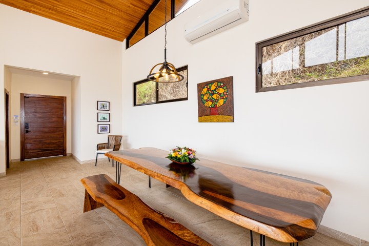 Room with a wooden table and bench, wall art, pendant light, and wood-framed windows.