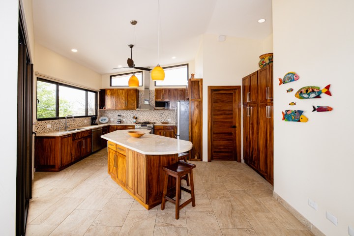 Spacious kitchen with wooden cabinets, island, tiled floor, pendant lights, and colorful fish wall decor.