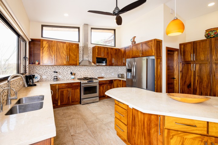 Modern kitchen with wooden cabinets, stainless steel appliances, island, and ceiling fan.