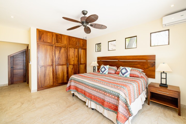 Bedroom with wooden furniture, colorful bedspread, ceiling fan, and small windows.