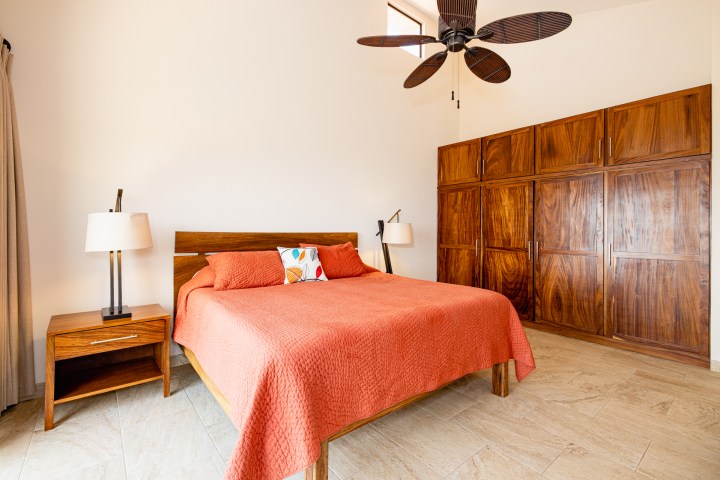 Bedroom with a wooden bed, orange bedding, bedside table, and large wooden wardrobe.
