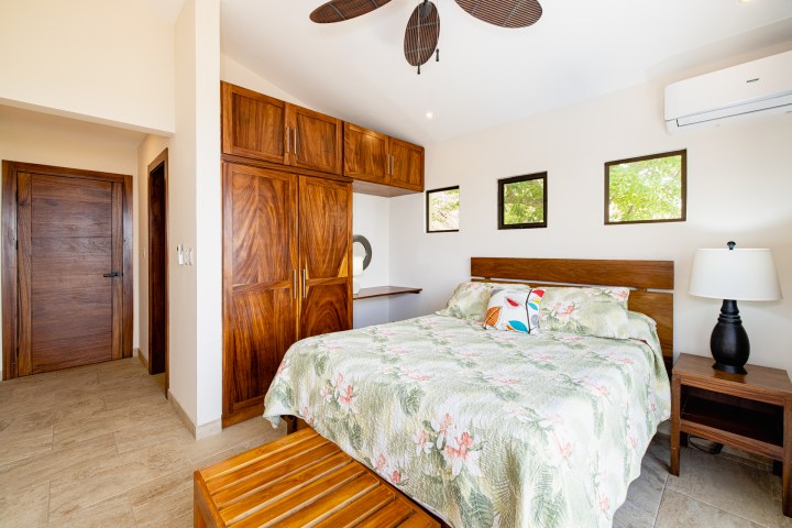 Bedroom with floral bedspread, wooden furniture, and three small windows.