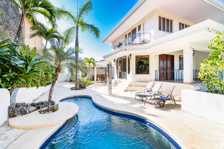 Tropical villa with pool, palm trees, and lounge chairs in the sunny backyard.