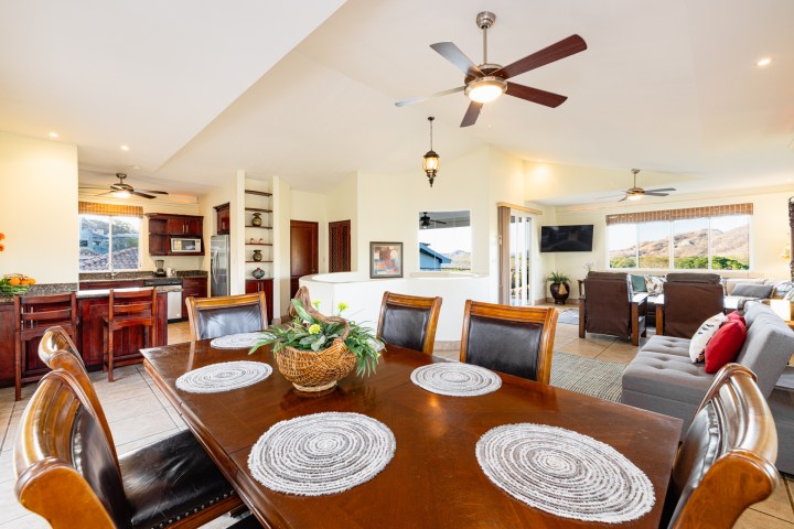 Open-plan kitchen, dining, and living area with ceiling fans and large windows offering a scenic view.