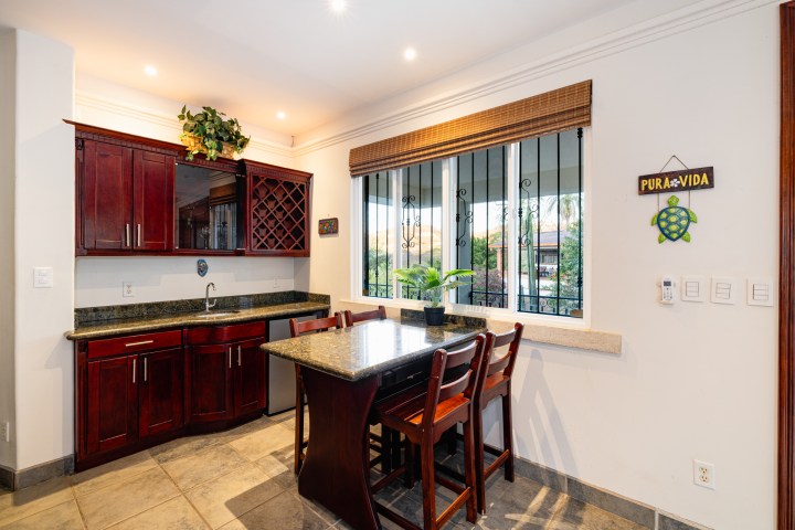 Kitchen with dark wood cabinets, dining counter, and window view, decorated with 'Pura Vida' sign and plant.