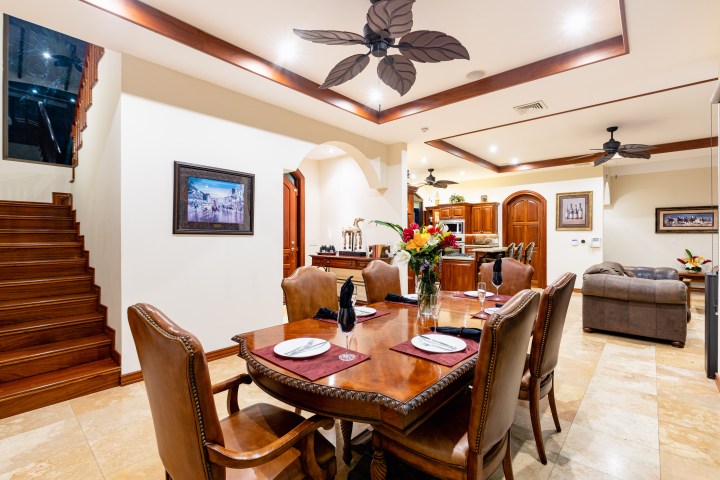 Elegant dining room with wooden table, chairs, stairs, and ceiling fans, leading to a cozy living room and kitchen.