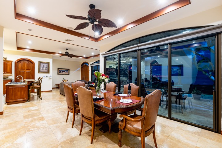 Elegant dining room with wooden table, leather chairs, ceiling fans, and large glass doors at night.