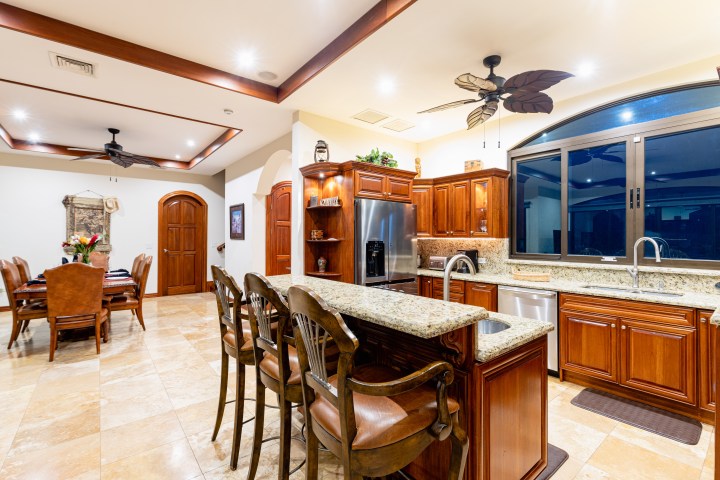 Modern kitchen and dining area with wooden cabinets and granite countertops, featuring ceiling fans and bar stools.