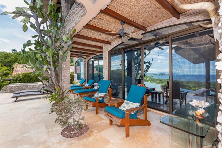 Outdoor patio with wooden chairs and blue cushions overlooking a scenic ocean view.