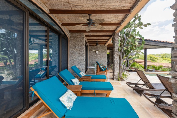 Outdoor patio with blue cushioned loungers, stone walls, and a pool view.