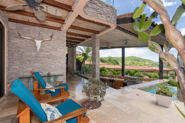 Patio with blue chairs, cow skull on stone wall, outdoor kitchen, and distant hills view.