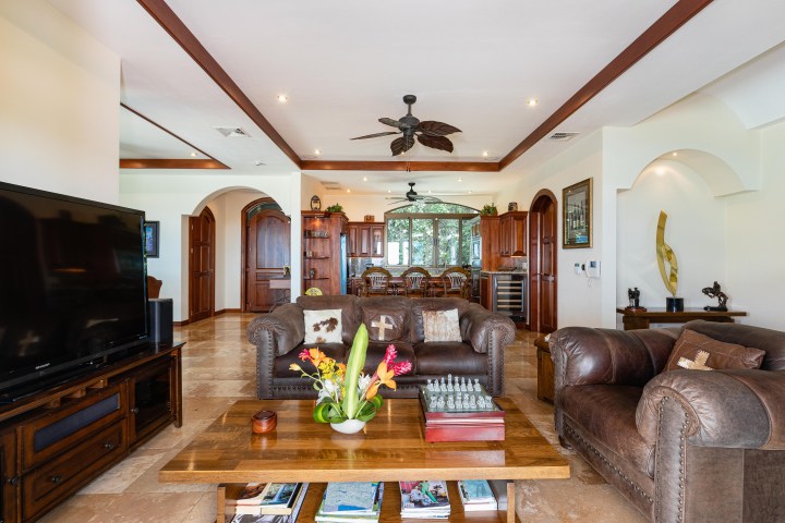 Spacious living room with leather sofas, large TV, wooden coffee table, and ceiling fan in a bright setting.