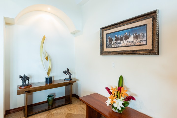 Corner with sculptures, a painting of horses, and a flower arrangement on tables.