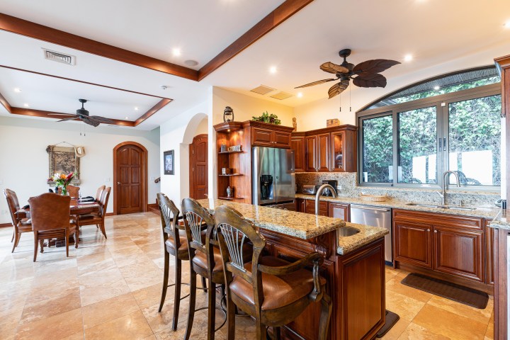 Open kitchen and dining area with wooden cabinets, bar stools, granite counters, and a ceiling fan.