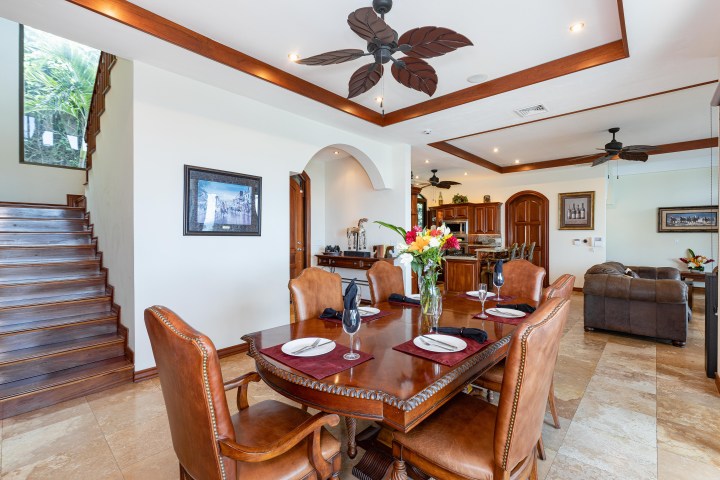 Elegant dining room with wooden table, leather chairs, flower centerpiece, and ceiling fan.