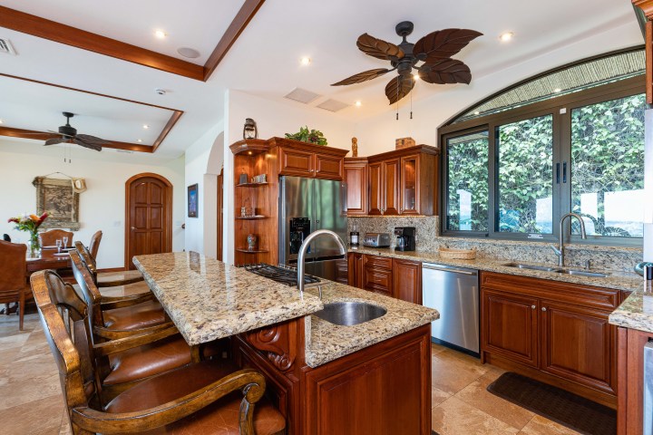 Luxury kitchen with granite island, wooden cabinets, stainless steel appliances, and leaf-shaped ceiling fans.