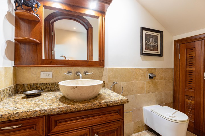 Bathroom with wooden cabinet, granite countertop, vessel sink, mirror, and toilet.
