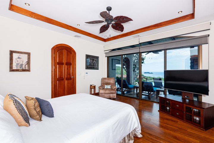 Bedroom with large bed, ceiling fan, and ocean view through sliding glass doors.