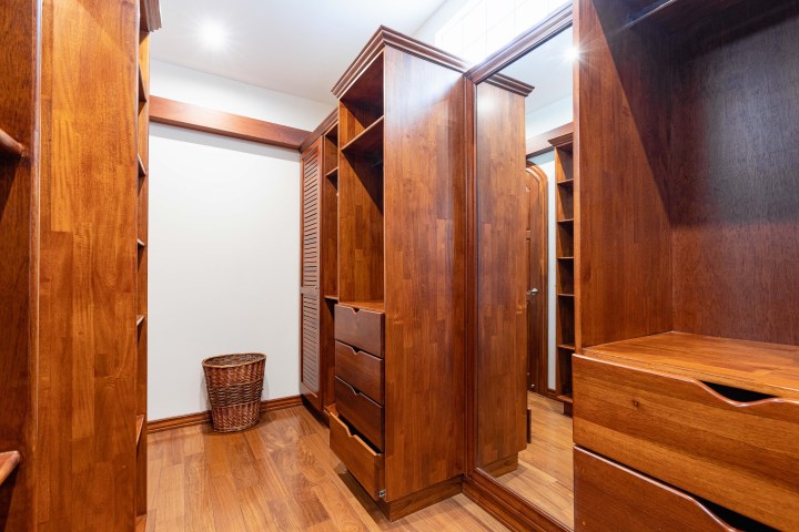 Wooden walk-in closet with mirrored doors and empty shelves, basket on the floor.