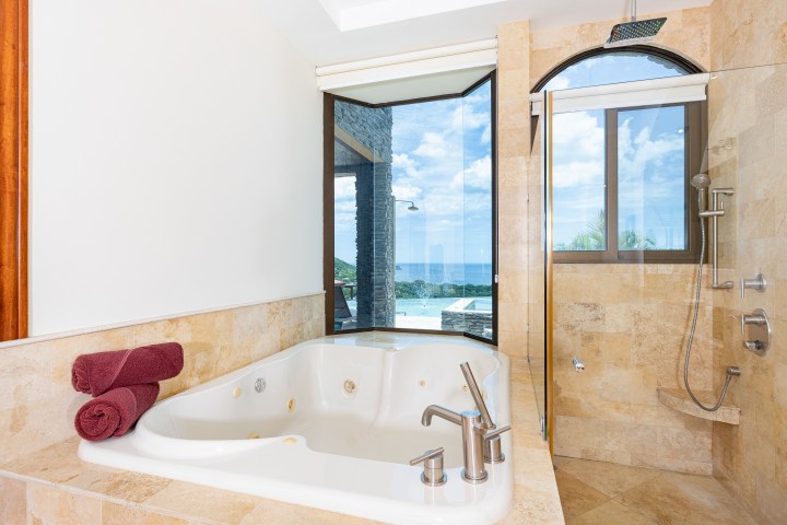 Luxurious bathroom with jacuzzi tub, shower, and large window with ocean view.