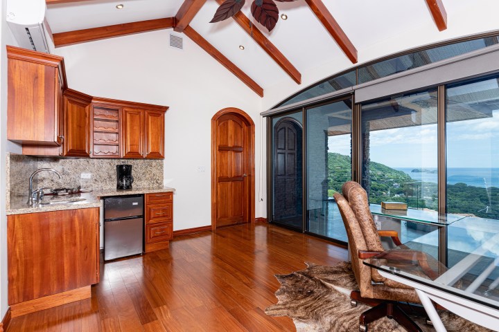 Room with wooden cabinets, mini fridge, glass doors, ocean view, and office chair by a desk.