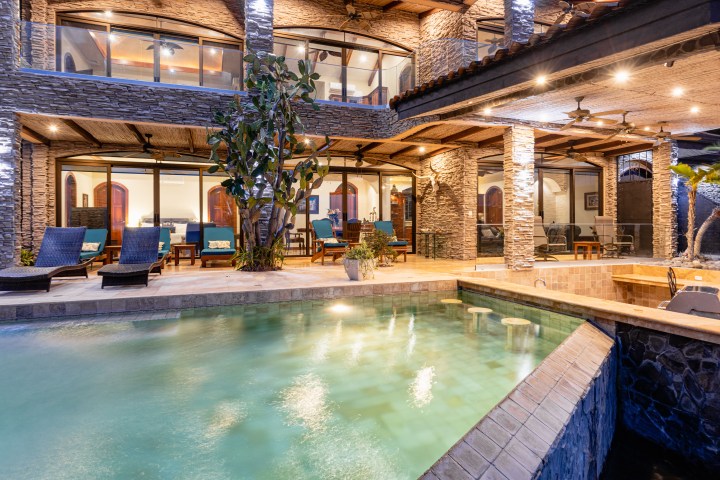 Luxury villa with stone facade, pool, and lounge chairs at night.