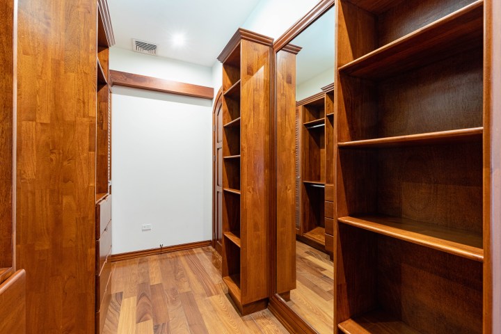 Wooden walk-in closet with built-in shelving and a large mirror.