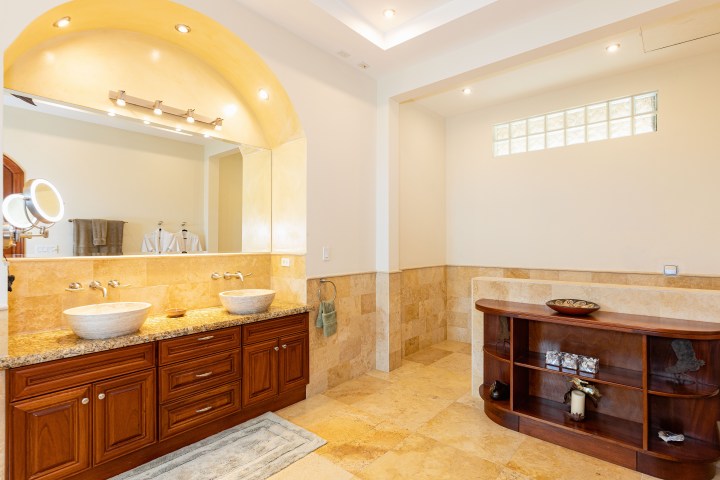 Luxurious bathroom with dual stone sinks, wooden vanity, and decorative shelves.