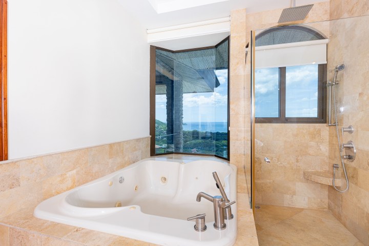 Luxurious bathroom with corner tub, glass shower, and ocean view from large windows.