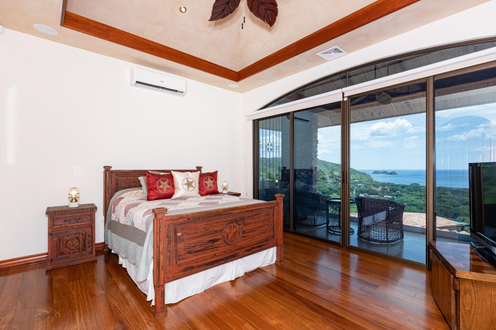 Bedroom with wooden bed, ocean view through large windows, and hardwood floors.
