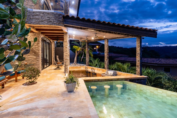 Luxurious patio with pool, stone walls, and furniture under a twilight sky.