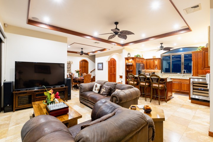 Spacious living room and kitchen with brown leather sofas, large TV, and wooden cabinetry.