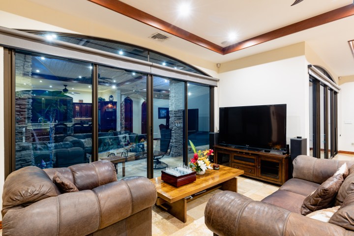 Modern living room with leather sofas, large TV, and glass doors showing a view of another room.