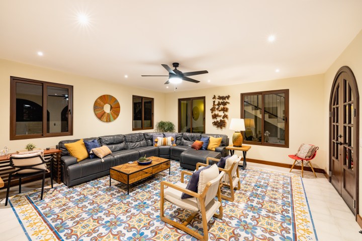 Spacious living room with a black sectional sofa, colorful cushions, patterned rug, and warm lighting.