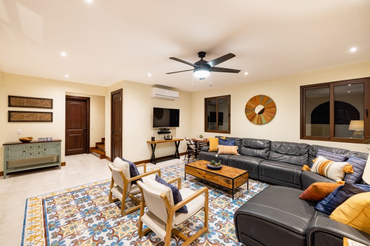 Living room with black leather sofa, patterned rug, and ceiling fan.