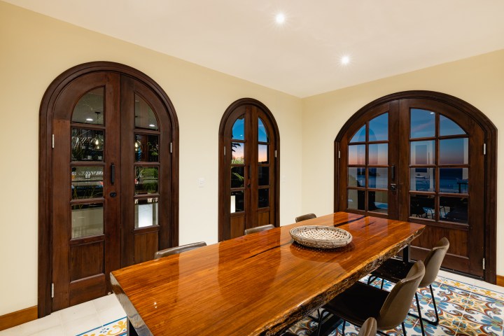 Dining room with wooden table, arched doors, and tiled floor at sunset.