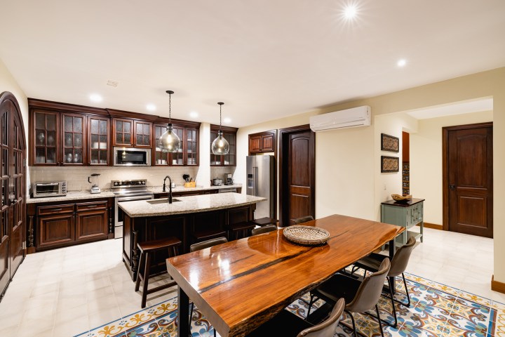 Elegant kitchen with wood cabinets, island, and dining table, under pendant lights.