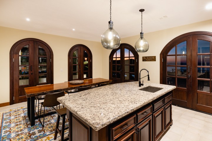 Kitchen with granite island, wooden dining table, arched doors, and pendant lights.