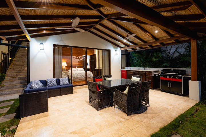 Covered patio with seating area, dining table, barbecue grill, and sliding glass doors to bedroom.