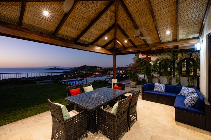 Covered patio with dining set and pool view facing the ocean at sunset.