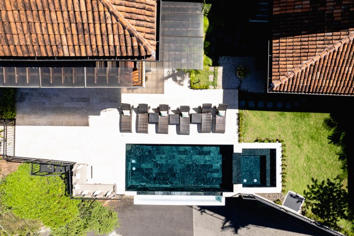 Aerial view of a modern pool area with sun loungers and surrounding tiled and grassy areas.