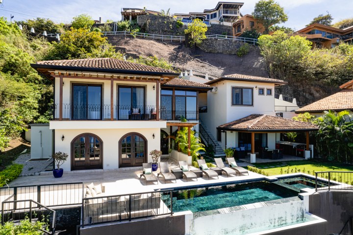 Modern villa with pool, sun loungers, large windows, and hillside view.